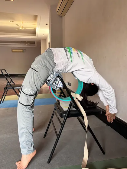 A student uses a chair and a yoga wheel to achieve a very deep backbend, demonstrating how props can assist in advanced flexibility training.