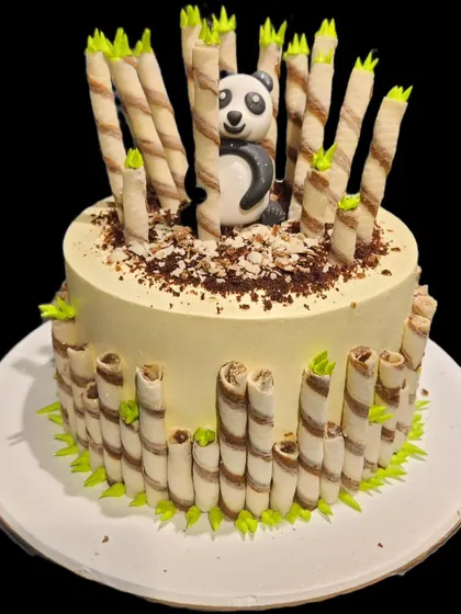An adorable panda cake set in a bamboo forest made of wafer rolls. This creative design features a cute fondant panda peeking out, making it a delightful and delicious centerpiece.