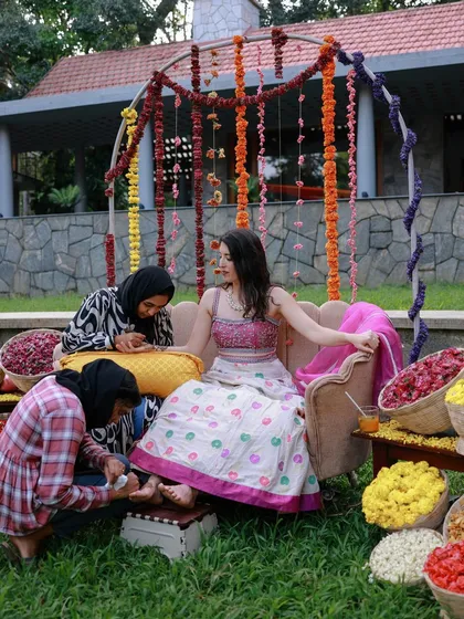 A classic Mehendi setup with the bride seated for her henna application, surrounded by baskets of fresh, colorful flower petals.
