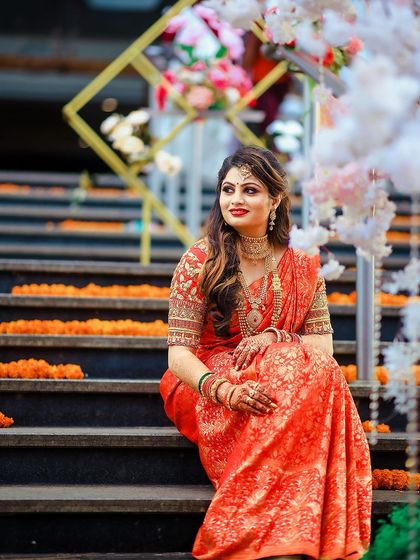A beautiful portrait of the bride-to-be seated on the steps, her red saree vibrant against the decor.