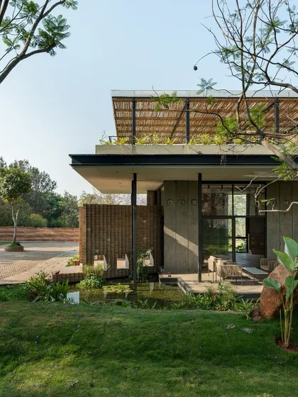 The building is designed with deep overhangs and verandas that create shaded outdoor spaces, surrounded by a water body and native plantings.