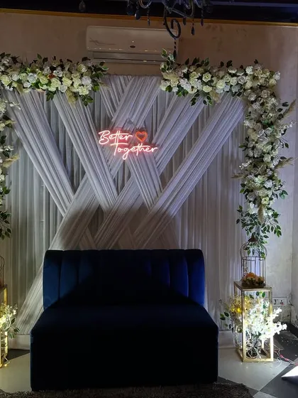 For modern engagement or roka ceremonies, I create clean and stylish backdrops. This setup uses white drapes, a floral arch, and a custom 'Better Together' neon sign for a chic photo corner.