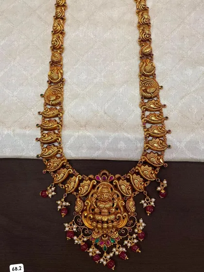 This 92.5 silver gold-plated necklace features a beautiful mango and peacock design. The large central pendant has a Goddess Lakshmi motif, making it a perfect piece of temple jewelry.