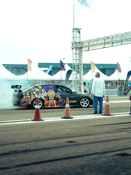 A custom-wrapped car prepares for launch, smoke billowing from the tires. This is the pre-race ritual, a spectacle of power and intimidation right at the starting line.