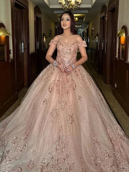 A full-length shot of a client in a hallway, wearing the sparkling rose gold ball gown. The dress fills the space with its volume and shimmer.
