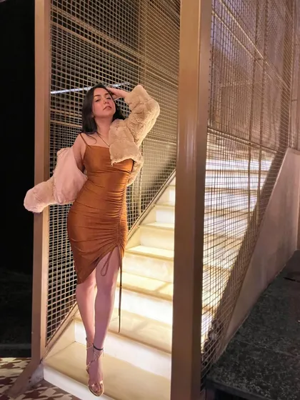 A dramatic pose on a lit staircase in a brown ruched dress and a fur jacket. This is a high-fashion, winter party look.