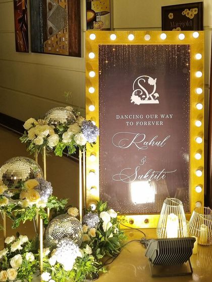 A glamorous welcome to a Sangeet night. We used a marquee-style sign with bulb lights, disco balls, and floral arrangements to set a "Black, White, and Gold" theme, promising a night of shimmer and dance.