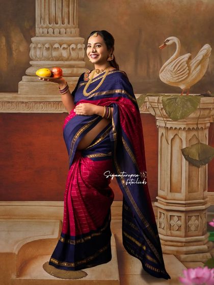 A full-length portrait in a stunning blue and pink saree, set against a classical, pillar-themed backdrop.