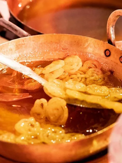 A chef prepares hot, crispy jalebis in a traditional copper kadai. This live dessert station fills the air with a sweet aroma, offering guests a classic Indian sweet made fresh.