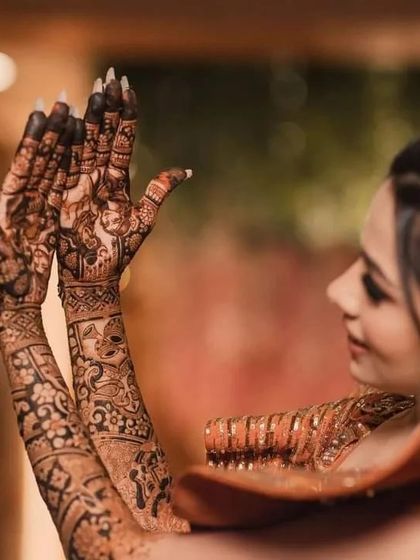 A side profile of a bride, showing the intricate mehndi design that extends all the way up her arms.