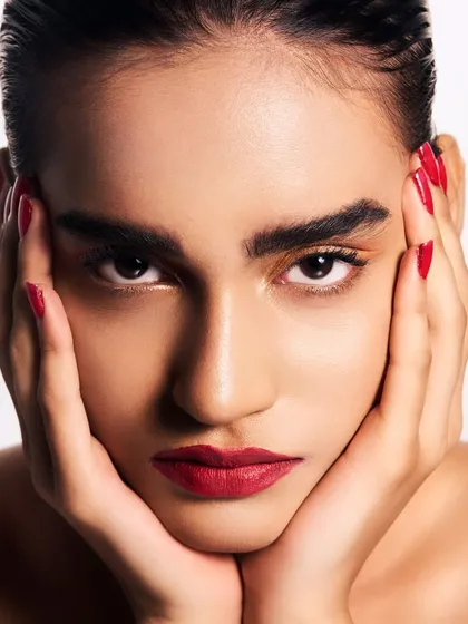 A beauty close-up focusing on a classic combination: a bold red lip and a touch of golden shimmer on the eyes. The hair is pulled back sleekly to keep the focus entirely on the face.