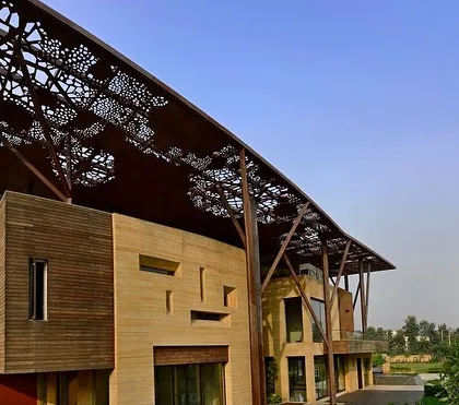 The Tree House facade combines teakstone walls with the dramatic, overarching metal canopy. The design plays with texture and form, creating a building that feels both monumental and intricately detailed.
