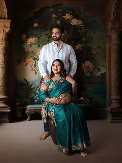 A regal couple's maternity portrait celebrating their journey to parenthood. The rich colors of the saree and the artistic painted backdrop create a timeless and elegant look in the studio.