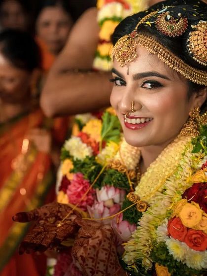 A stunning portrait of a South Indian bride, adorned with traditional jewelry and flower garlands, smiling directly at the camera. We capture the beauty and grace of our brides.
