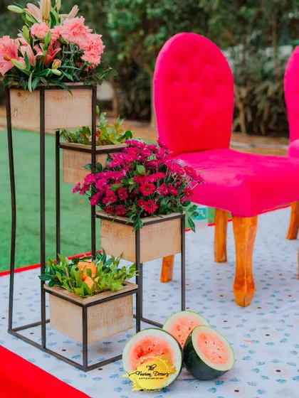 A vibrant pink chair stands out against the fresh green grass, with tiered planters holding colourful flowers and fresh watermelons adding a playful touch.