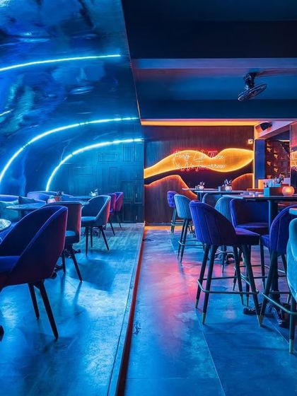 The lounge area of a bar we designed, featuring dramatic blue and pink neon lighting that reflects off the ceiling. The design creates a gorgeous, immersive atmosphere that is perfect for a night out.