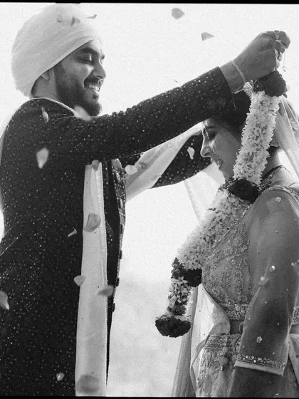 The Varmala ceremony, captured in timeless black and white. The falling petals and the couple's smiles create a dynamic, emotional image of this key wedding moment.