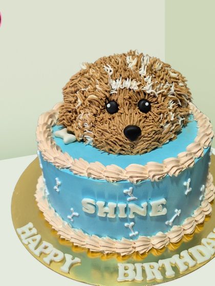 An adorable 3D puppy cake that's almost too cute to eat. The puppy's head is sculpted from cake and frosting, popping out of a blue base, perfect for any dog lover's birthday.