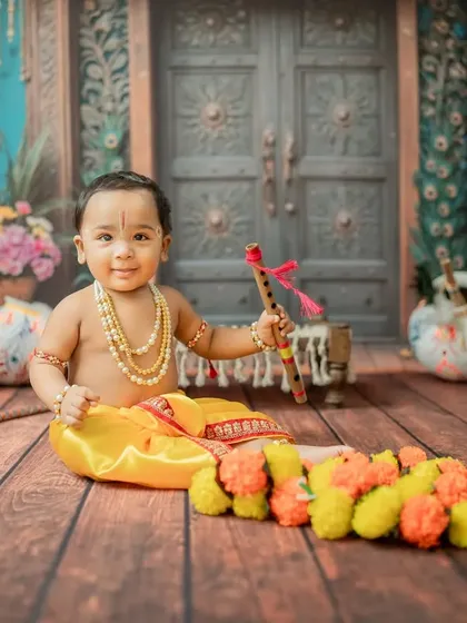 A charming Little Krishna sitting with his flute, surrounded by marigold garlands and traditional pots.