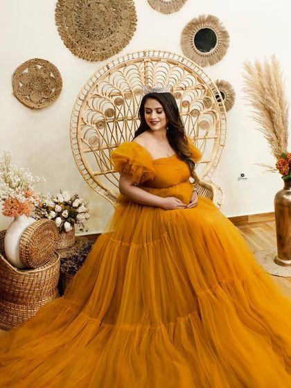 A serene moment captured in the boho-themed setup. The client, seated in the peacock chair, looks down lovingly at her bump, creating a sweet and intimate portrait.