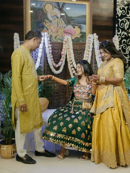 A beautiful family moment during the Mehendi ceremony. The decor, with its intricate wooden screen and floral garlands, provides a warm and traditional setting for these precious interactions.