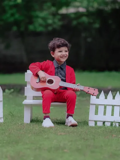 A future rockstar. His joyful smile while strumming a tiny guitar is absolutely infectious. The simple white picket fence and green grass create a perfect stage for his outdoor portrait session.