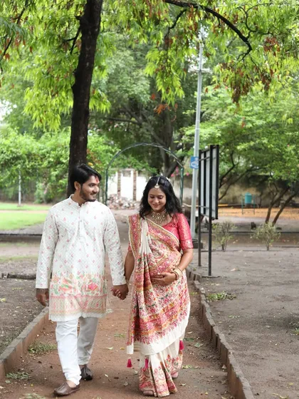 A beautiful outdoor shot of the couple at their baby shower celebration. The mom-to-be is glowing in a traditional saree with soft, elegant makeup.