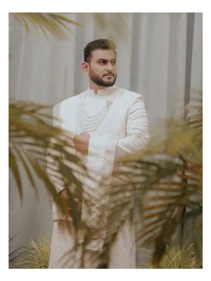 Elegance captured. This groom wears a custom all-white sherwani, featuring intricate chikankari work and layered pearl necklaces, creating a look of serene royalty for his special day.