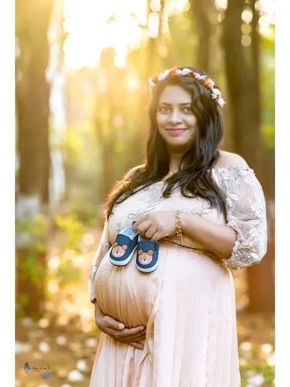 A serene solo portrait captured during the magical golden hour. The warm, soft sunlight beautifully highlights the mother's glow as she holds a pair of baby shoes, looking forward to the new chapter ahead.