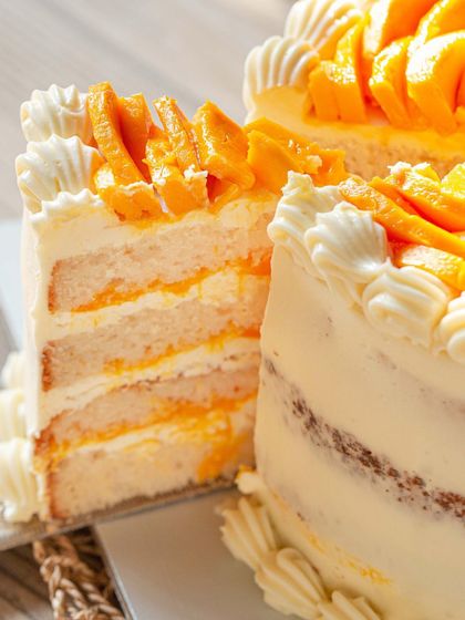 A close-up slice of the Vanilla & Mango Cake, revealing the soft cake layers and the generous filling of fresh mango and cream.