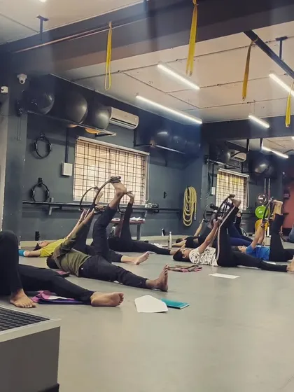 A group of students works on hamstring stretches using Pilates rings, demonstrating the integration of different fitness disciplines.