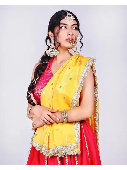 The vibrant contrast of pink and yellow in this traditional attire is the focus here. The clean white background makes the colours pop, while the model's pose highlights the beautiful drape of the dupatta and the statement jewellery pieces.