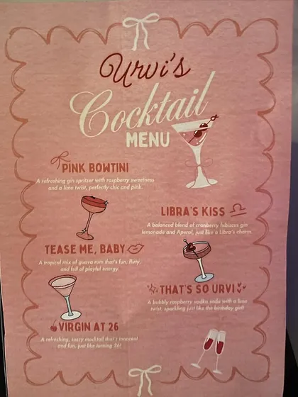 The custom-designed pink cocktail menu for Urvi's 26th birthday, with fun, personalized drink names like 'Libra's Kiss' and 'That's So Urvi'.
