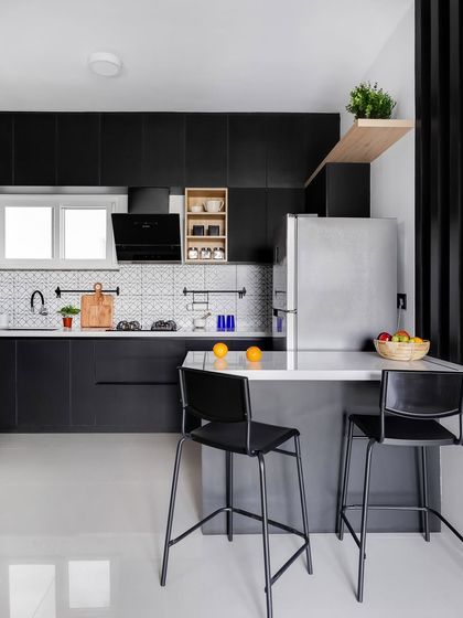 For a bold, modern look, this kitchen features all-black cabinetry. A patterned tile backsplash adds a graphic element, while a simple wooden shelf provides a touch of warmth and a place for everyday items. The island doubles as a breakfast bar.