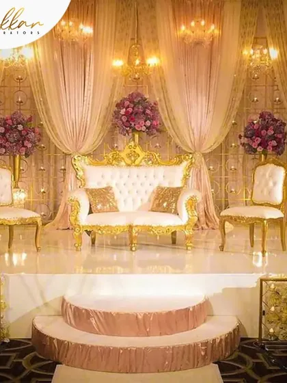 A classic and elegant reception stage with a pink and gold theme. The royal seating and soft, draped backdrop create a timeless and romantic atmosphere.