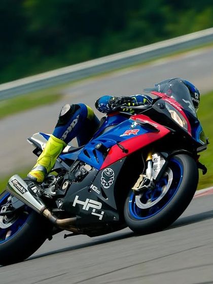 The iconic colors of a BMW HP4 race bike stand out against the tarmac as the rider navigates a sweeping corner.