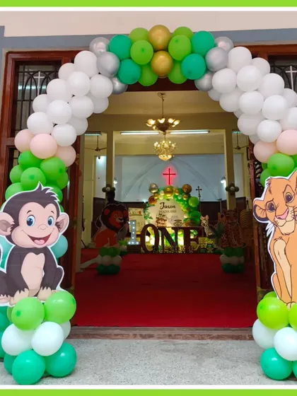 A grand balloon archway welcomes guests to a jungle-themed first birthday. Character cutouts of Simba and a monkey stand at the entrance, setting the stage for the wild adventure inside.