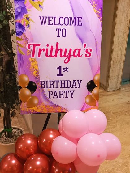 A welcome easel stand for a first birthday party, with a custom-designed sign and a small balloon cluster at the base.
