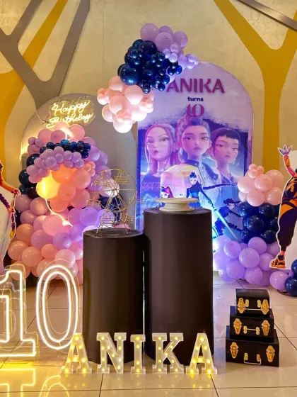 A detailed shot of the 'Huntrix' themed birthday setup. You can see the custom-printed backdrop, coordinated plinths, and marquee letters, all working together to create an immersive experience.