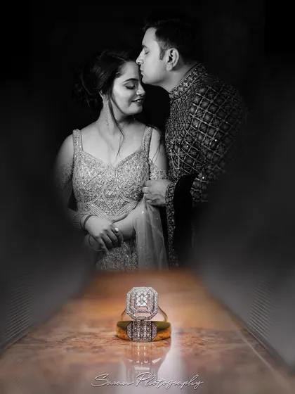 An artistic shot focusing on the engagement rings, with a black and white portrait of the couple in the background.