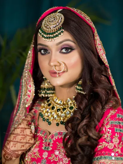 A vibrant look for a bride in a bright pink and red lehenga. The eye makeup has hints of pink and purple, and her hair is styled in soft waves.