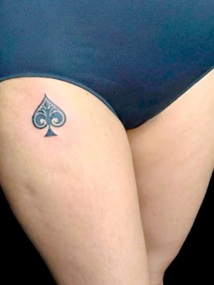 A spade symbol tattoo on the upper thigh.
