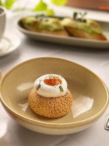 A delicate choux pastry with a craquelin top, filled with cream and topped with a dollop of fruit jam. This is served in a bowl, ready to be enjoyed in our cozy cafe.