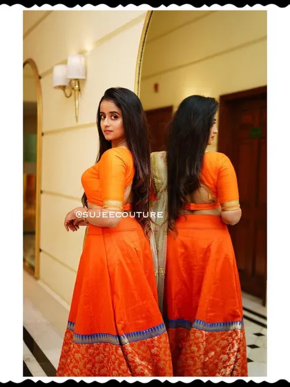This view highlights the modern, deep-back design of the blouse for the orange lehenga worn by Chaitra Vasudevan, adding a contemporary touch to the traditional ensemble.
