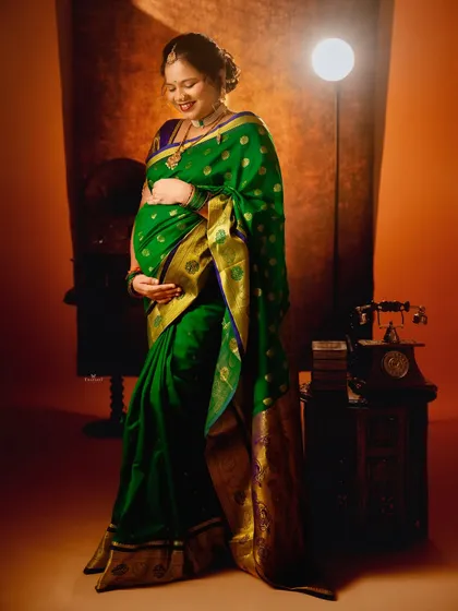 A full-length portrait showcasing the beautiful drape of a green silk saree. The soft lighting and vintage props add to the classic feel of the shot.