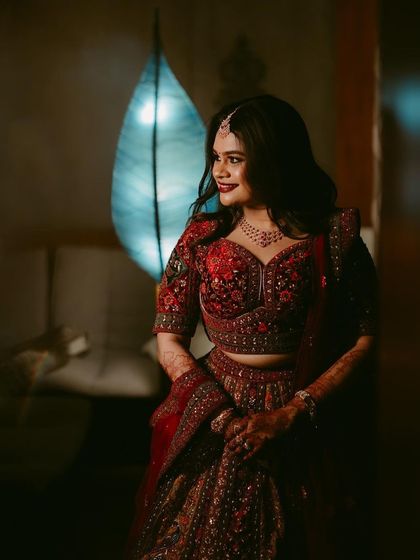A stunning bridal portrait in a richly embroidered red lehenga. The moody lighting and the bride's confident glance create a powerful and glamorous feel.