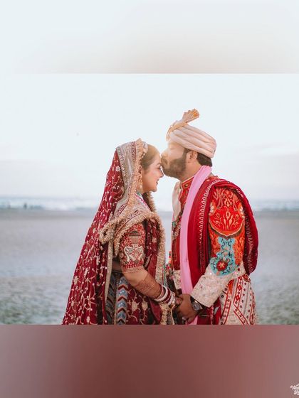 A romantic portrait of the groom kissing the bride's forehead against the serene backdrop of the sea.