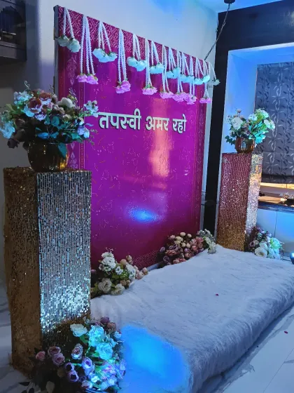 A shimmering pink backdrop for a Jain ceremony. The setup includes a comfortable floor seating area on a white fur rug, flanked by sequined pillars and flower vases.