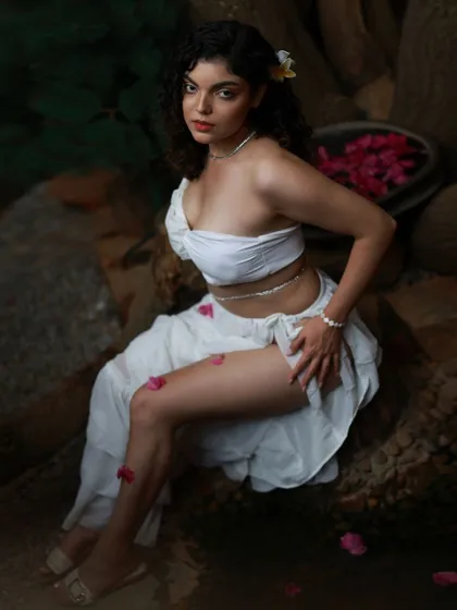 A seated portrait from the Apsara series. The pose is elegant and powerful, and the scattered petals on the rocks add a touch of delicate beauty.