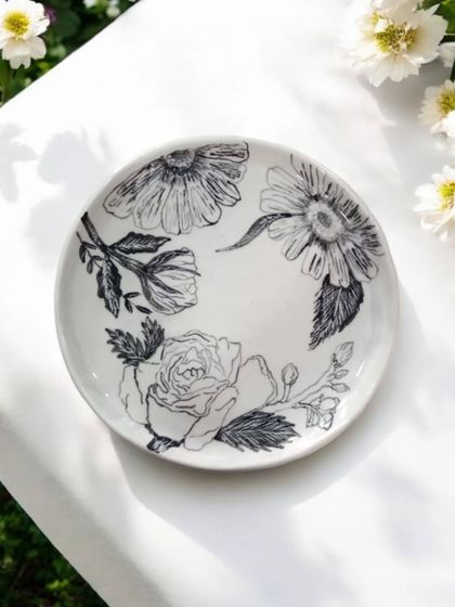 A handmade ceramic plate with a delicate floral sketch design, pictured in natural light. Each plate is a piece of functional art, celebrated for its unique craftsmanship and artistic value.